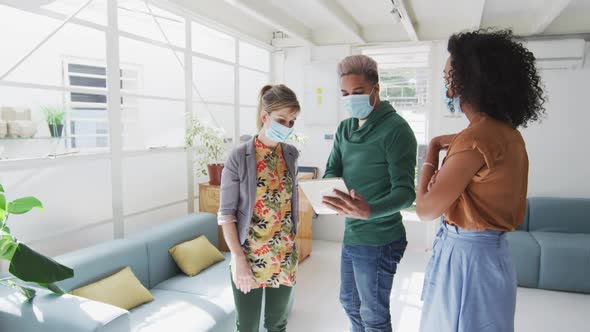 Office colleagues wearing face mask discussing over digital tablet at office