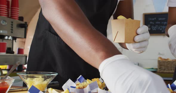Mid section of african american man wearing apron putting fries in a box in the food truck