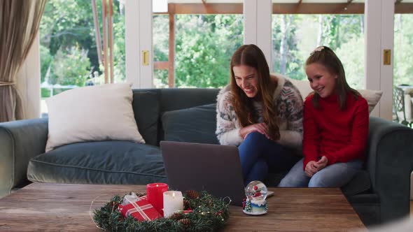 Caucasian mother and daughter smiling and waving while having a video call on laptop sitting on the