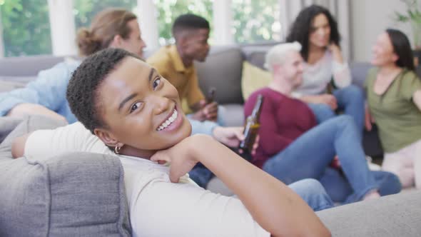 Smiling biracial woman sitting with diverse group of happy friends socialising in living room