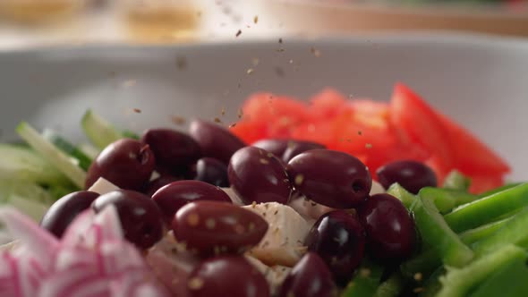 Camera follows putting oregano herb over greek salad. Slow Motion.