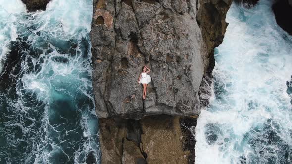 Woman in a White Short Dress Lies on the Edge of a Cliff