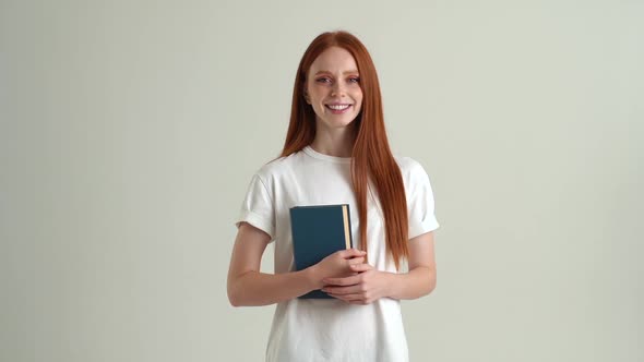 Portrait of Smiling Pretty Young Student Woman Holding in Hands Paper Book and Looking at Camera