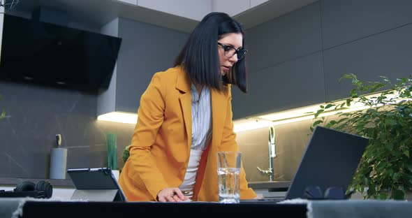 Woman in Glasses and Business Clothes Standing Near Kitchen Table and Writing Down Important Notes