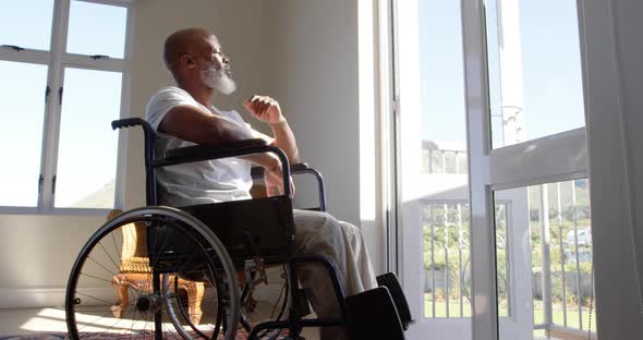 Side view of mature black handicap man sitting on wheelchair near the window at home 4k