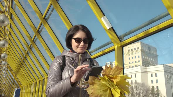 A Middleaged Woman Brunette Caucasian with Short Hair with a Bouquet of Yellow Leaves Walks Along