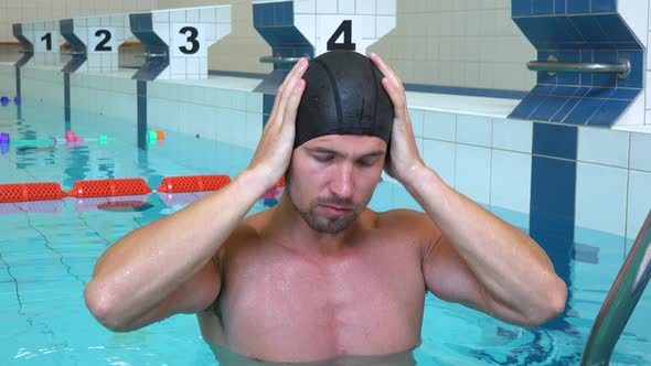 A Professional Swimmer Puts on a Cap and Goggles and Smiles at the Camera in an Indoor Pool