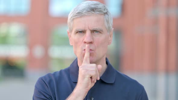 Outdoor Portrait of Middle Aged Man Putting Finger on Lips