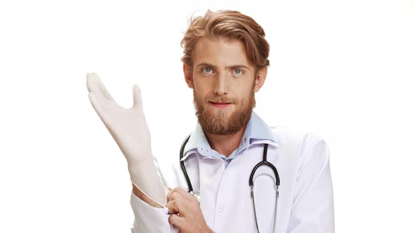 Ready Young Caucasian Male Doctor with Light Beard and Medical Overall Smiling Wearing Disposable