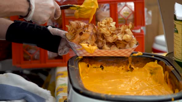 Slow motion of putting cheese sauce on a serving of tornado or curly potato fries.