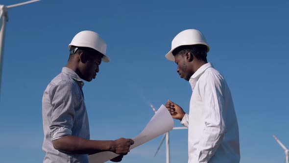 Two Male African American Electrical Engineers Stand Against the Backdrop of a Windmill at an Air