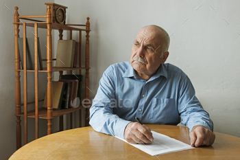 a paper document on the table in front of him as he looks to the side with a thoughtful engrossed expression