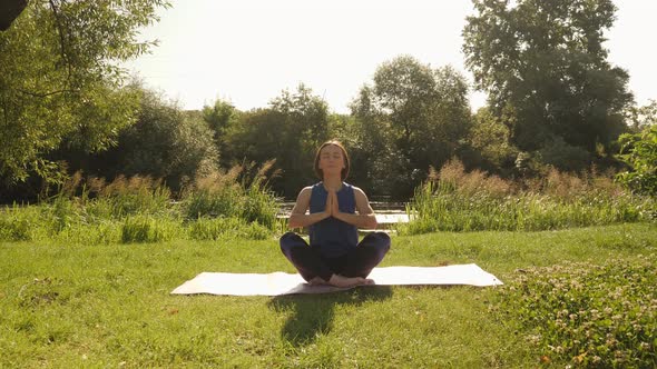 Young lady doing yoga exercises at forest. Woman practicing yoga in summer park at sunrise.