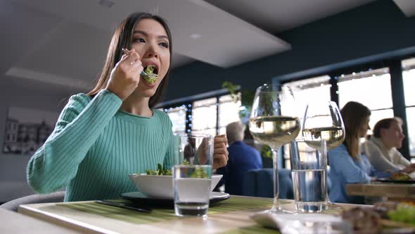 Asian Woman Eating and Communicating in Restaurant