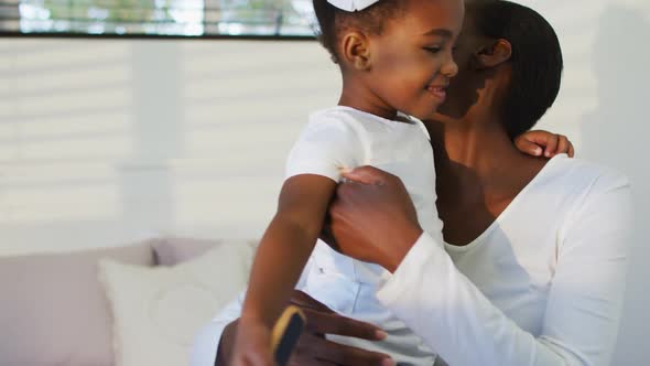 Happy african american mother and daughter sitting on bed and hugging