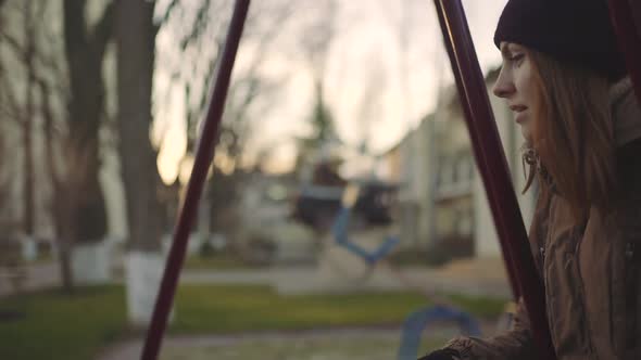 Young Attractive Redhaired Woman Swinging on a Swing in the City at Sunset or Sunrise