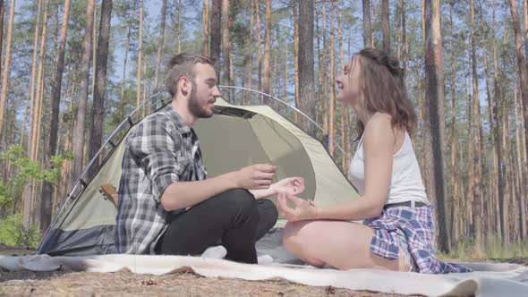 Portrait Young Man and Woman Sitting in Front of Each Other in Forest Meditating. The Tent on the
