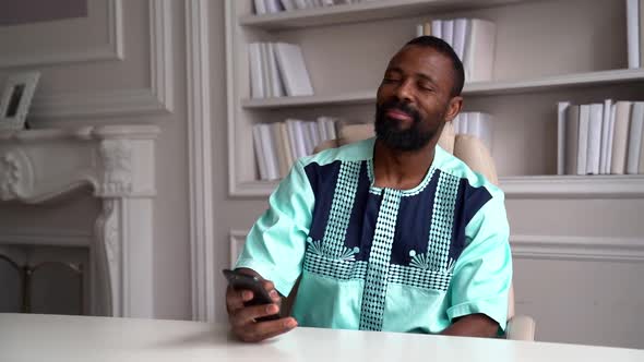 Middle-aged African-American Man in a T-shirt. The Businessman Is in a Bright Office, He Looks at