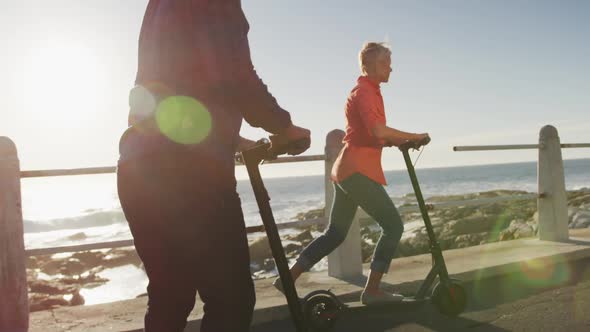 Senior couple using electronic scooters alongside beach