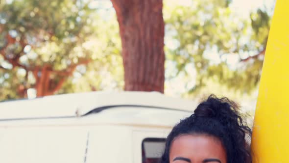 Smiling woman with surfboard standing near camper van 4k