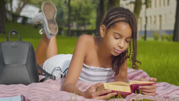 Happy Intelligent Little Girl Reading Book and Smiling at Camera. Portrait of Joyful African