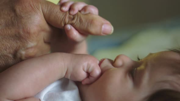 Slow Motion of Baby with Hand in Mouth and Holding Grandfather's Finger