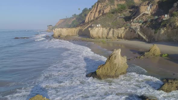 Aerial shots of El Matador beach over breaking waves and rocks on a hazy summer morning in Malibu, C