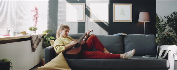Woman Playing Guitar on Sofa in Living Room