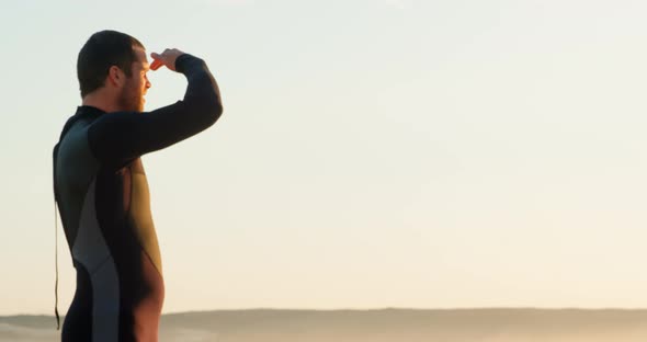 Side view of mid-adult caucasian male surfer with shielding eyes looking at sea at beach 4k