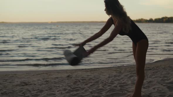 Young Woman Prepares Her Yoga Mat for an Evening Training at Lake