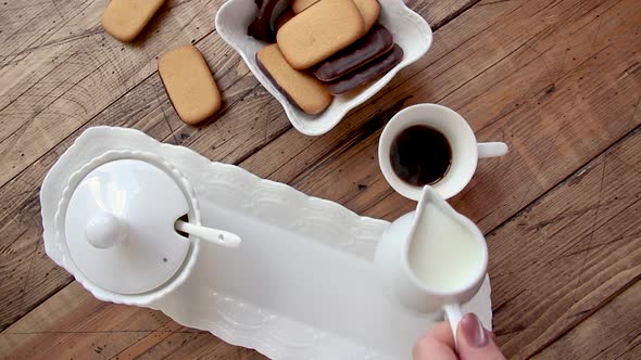 Hand pouring milk into a coffee on a wooden table top view