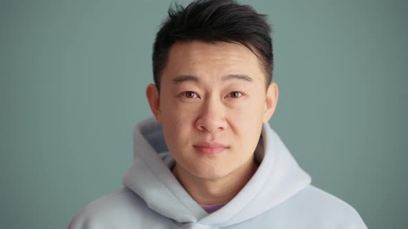 Smiling Asian man wearing hoodie opening his eyes at the camera