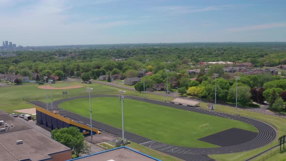 High school bleachers and track in residential neighborhood with city skyline on the horizon- aerial