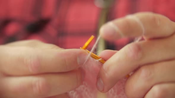 A Woman Knits a Piece of Clothing From a Thin Pink Yarn