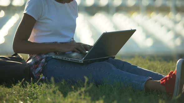 African American Student Typing on Laptop, Sitting on Lawn, Working on Project