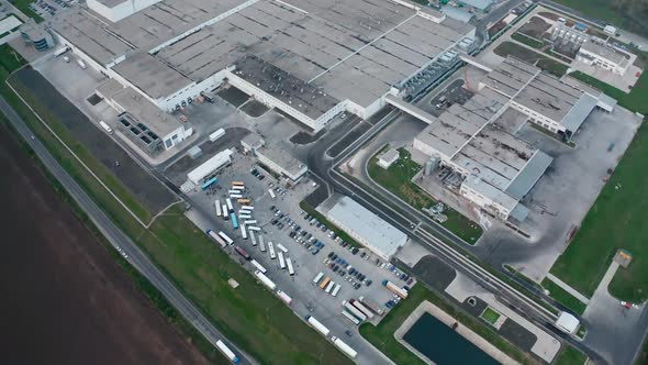 Factory on field near the road. Large production plant with car parking nearby. 