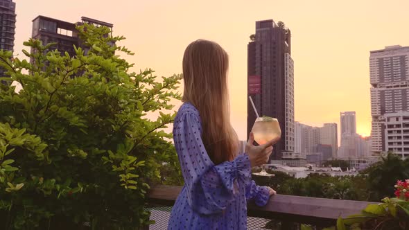 Back View of Young Woman on Rooftop Drinking Orange Cocktail Enjoy Sunset