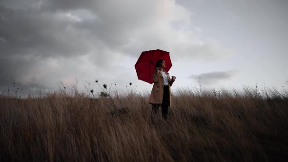 Woman with trench cost and red umbrella in a field in the nature