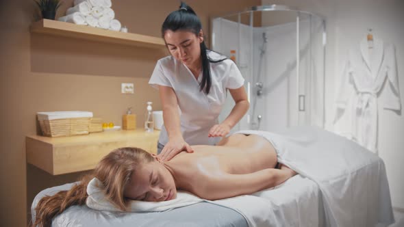 Woman Receiving a Massage  Lying on the Couch While the Masseuse Spreads the Oil on Her Skin