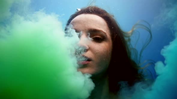Young Lady is Floating in Pool Clouds of Green and Blue Paints are Covering Her Face and Hair