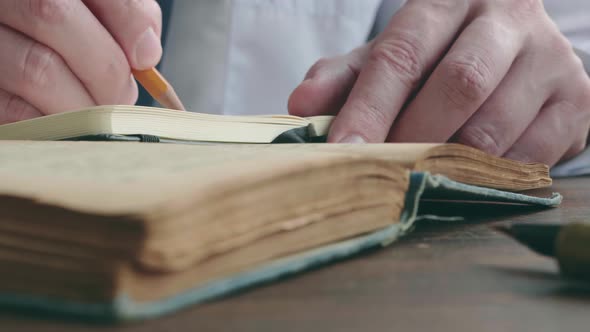 Closeup of a Pencil Writing in a Notebook Next to an Old Book