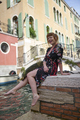 Caucasian redhead woman with floral dress sitting near a canal in Venice - PhotoDune Item for Sale