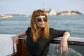 Redhead girl with long black dress, sunglasses and cowboy boots standing on yacht in Venice - PhotoDune Item for Sale