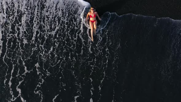 Top View of a Woman in a Red Swimsuit Lying on a Black Beach on the Surf Line. Coast of the Island