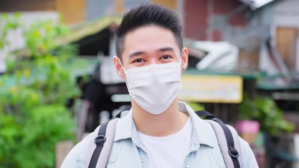 Portrait of Asian attractive male backpacker wear mask travel in city.