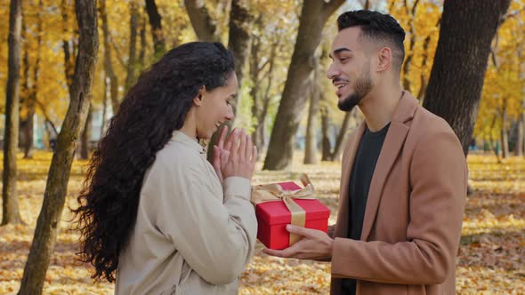 Hispanic Handsome Bearded Man Gives Gift Large Red Box with Gold Ribbon Excited Attractive Young