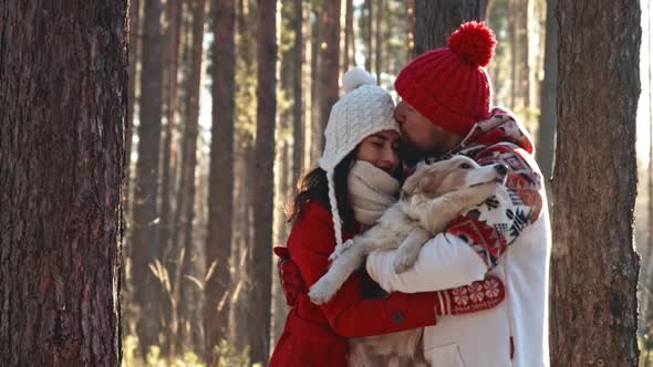 Happy Young Couple Hugging in Winter Forest with Their Doggy