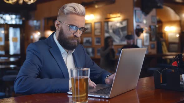 Young Businessman Drinking Beer While Using Laptop in Restaurant