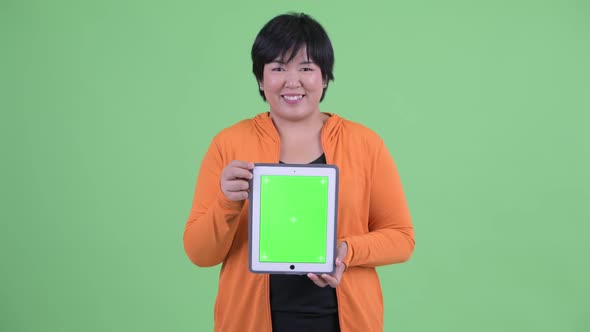 Happy Young Overweight Asian Woman Thinking While Showing Digital Tablet Ready for Gym