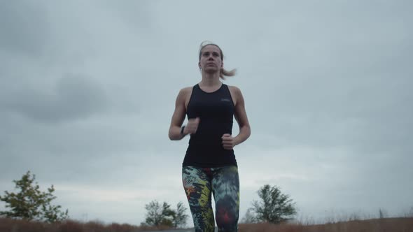 Running female athlete runs against a cloudy sky in sportswear with a fitness bracelet.